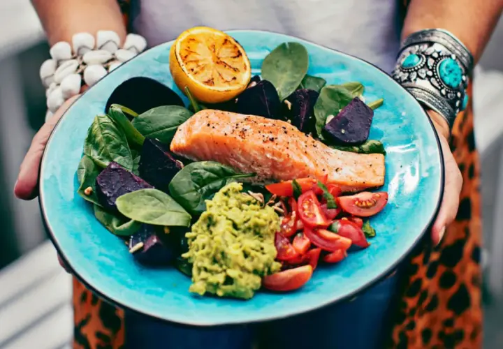 En matig sallad med lax, rödbetor, spenat, tomat, avokado och grillad citron på en turkos tallrik.