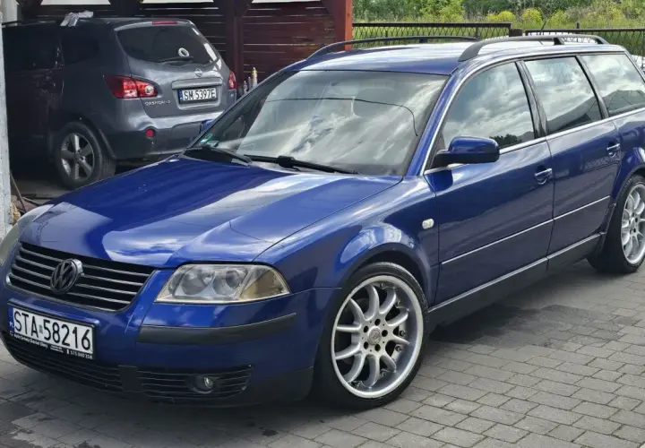 Błękitny Passat B5 1.9 TDI 130KM na aluminiowych felgach, zaparkowany na podjeździe obok szarego SUV-a.