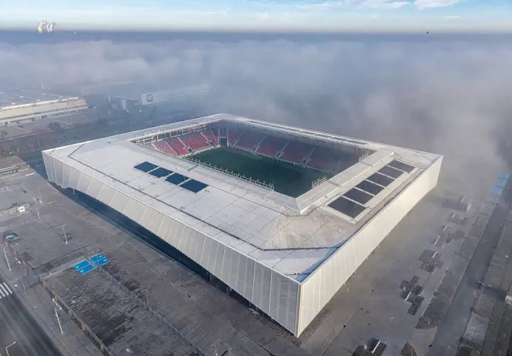 Nowy stadion Odra Opole wyłania się z mgły. Nowoczesna bryła z panelami słonecznymi i czerwonymi trybunami.