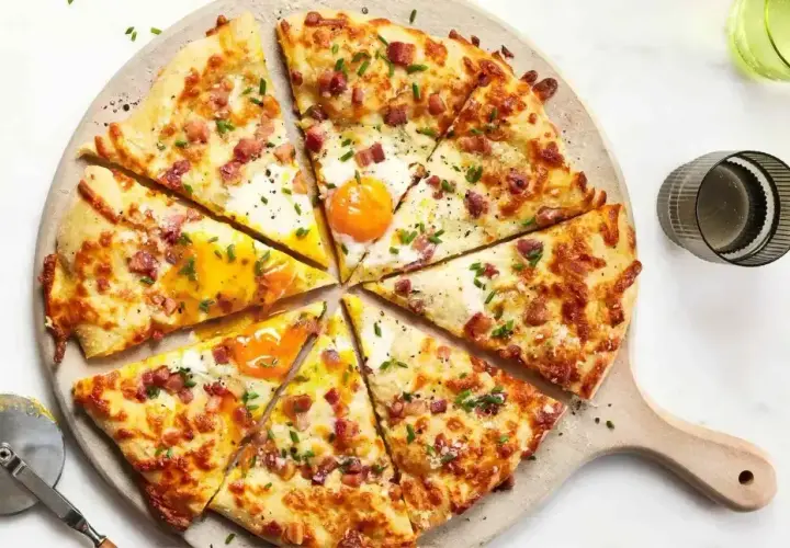 Kawałki pizzy carbonara z jajkiem sadzonym, boczkiem i szczypiorkiem na desce.