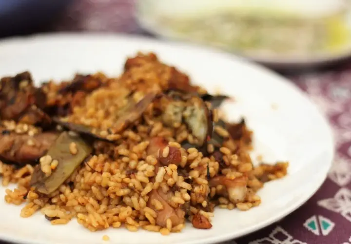 Deliciosa paella de conejo con trozos de carne dorada y verduras, servida en un plato blanco.