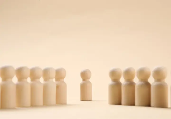 Un pupazzetto di legno si erge da solo, separato da un gruppo. Un simbolo di imparare a stare da soli, trovando forza nella propria individualità.