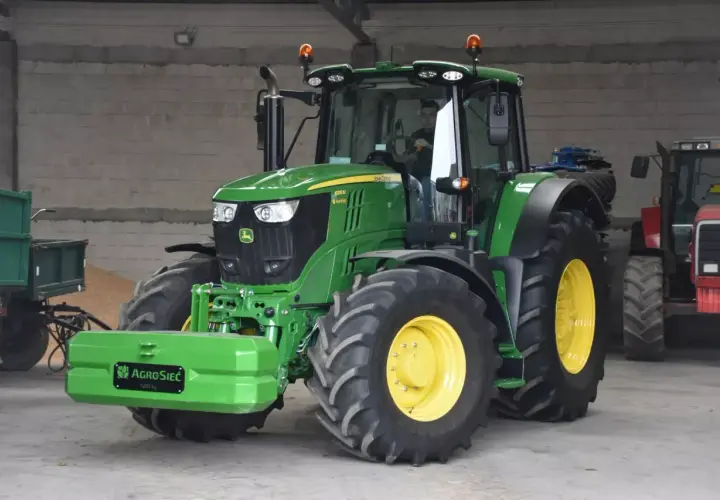 Zielony John Deere 6195M, z kierowcą w kabinie, stoi obok przyczepy. Czy to najlepsza marka ciągnika?