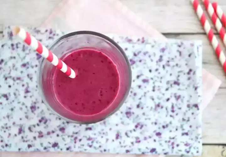 En glas med en lila indisk yoghurtdryck, med ett rött och vitt randigt sugrör.