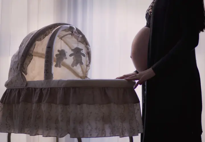 Gravid kvinna med händerna på en vagga med nallar, en fixerad bebis väntar.
