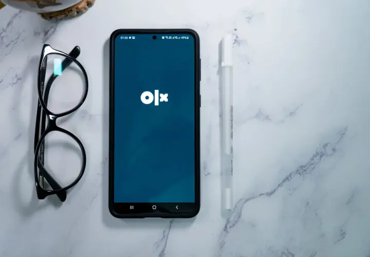 Telefon z aplikacją OLX, okulary i długopis na marmurowym tle. Dowiedz się, jak dodać ogłoszenie na OLX za darmo.