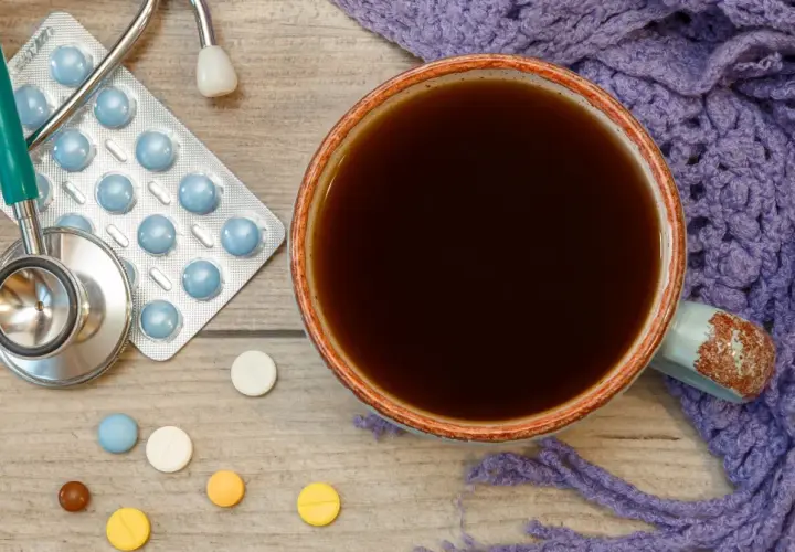 Tasse Kaffee, Stethoskop, Pillen und eine lila Decke. Vielleicht ist es Zeit für die **Selen Einnahme** und einen warmen Kaffee.