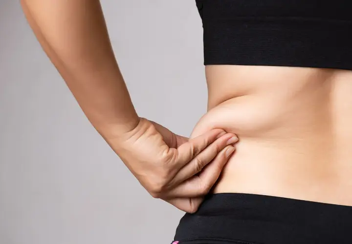 En hand som klämmer på fett på sidan av midjan, en vanlig indikation för coolsculpting.
