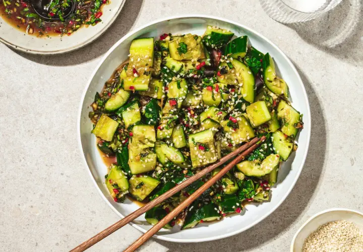En skål med krossad gurksallad, toppad med sesamfrön och färska örter, redo att avnjutas med ätpinnar.