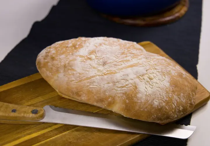 Nybakat bröd med en kniv på en skärbräda. Doften av nybakat bröd sprider sig i köket.