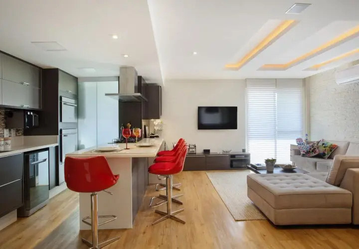Cucina moderna con isola e sgabelli rossi, soggiorno con divano e TV. Il soffitto in cartongesso design crea un'atmosfera accogliente.