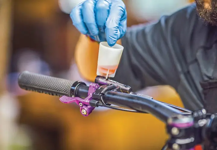 Gloved hand pours fluid into a bike's brake lever, a step in learning how to bleed hydraulic lines.