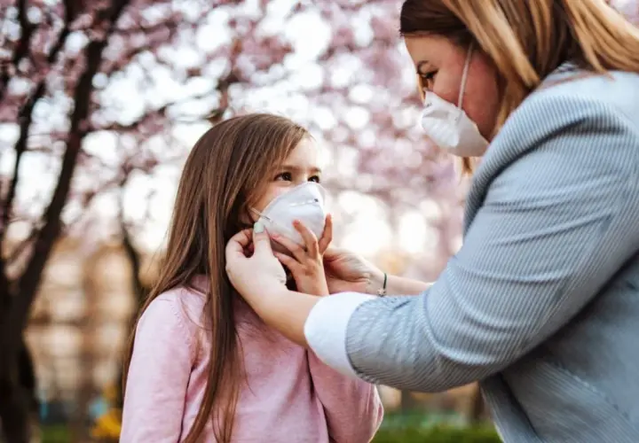 Madre ajusta mascarilla FFP2 a su hija bajo un árbol en flor. Una mascarilla FFP2 para que sirve, protege eficazmente.