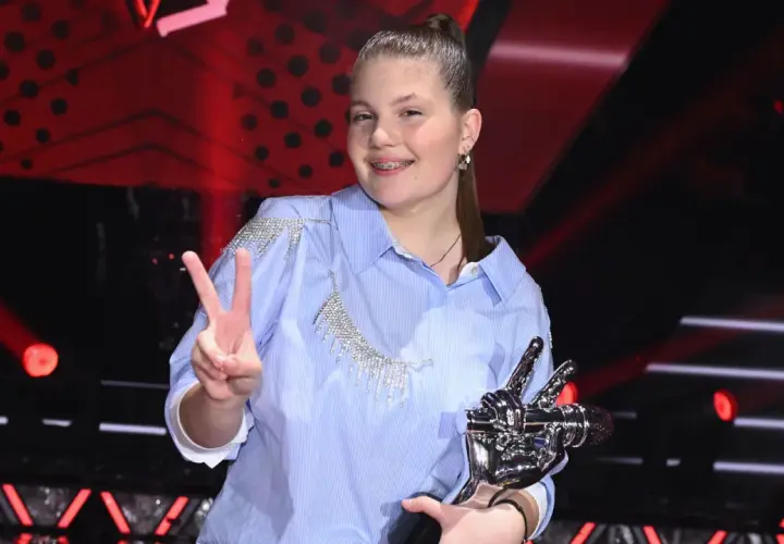 Młoda artystka z pucharem i znakiem pokoju, radośnie świętuje zwycięstwo w The Voice Kids.