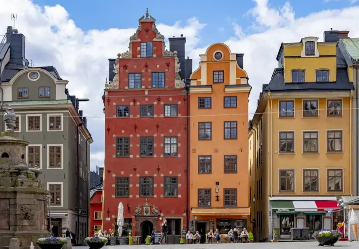 Färgglada hus på Stortorget, Stockholm sommar. En fontän står framför de gamla byggnaderna.