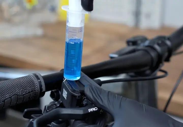A syringe filled with blue fluid is used to bleed the brakes on a bicycle.