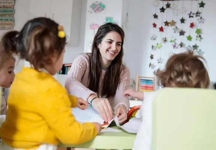 Eine Kinderpflegerin lächelt, während sie mit Kindern bastelt. Sie fragt sich, wie viel verdient man als Kinderpflegerin?