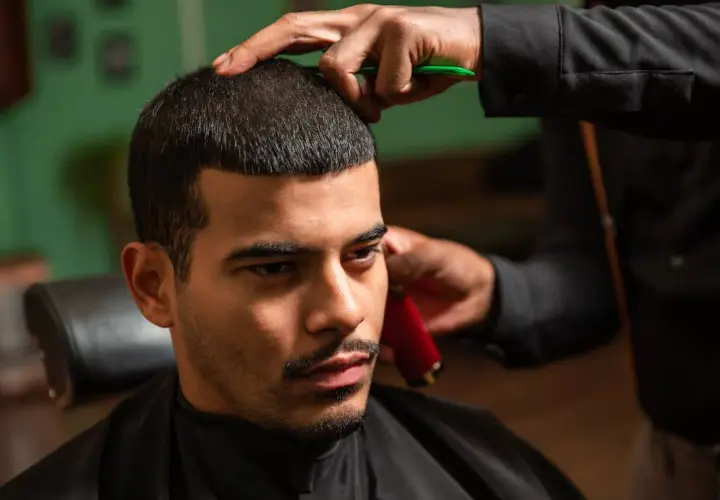 Mann bekommt einen Buzz Cut 15mm. Der Friseur trimmt das Haar mit einer Schere und einem Trimmer.