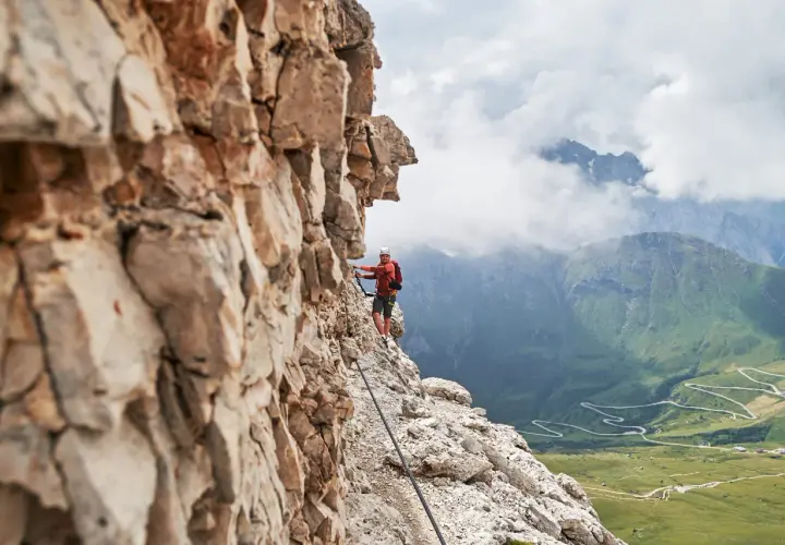 Wspinacz na via ferrata w Dolomitach, z widokiem na kręte drogi i zielone doliny.