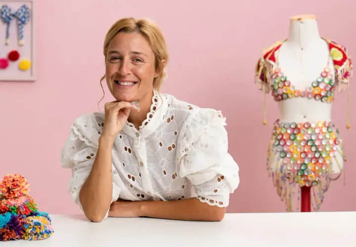 Mujer sonriente junto a un maniquí con un traje colorido de upcycling moda. Montón de pompones de colores a la izquierda.