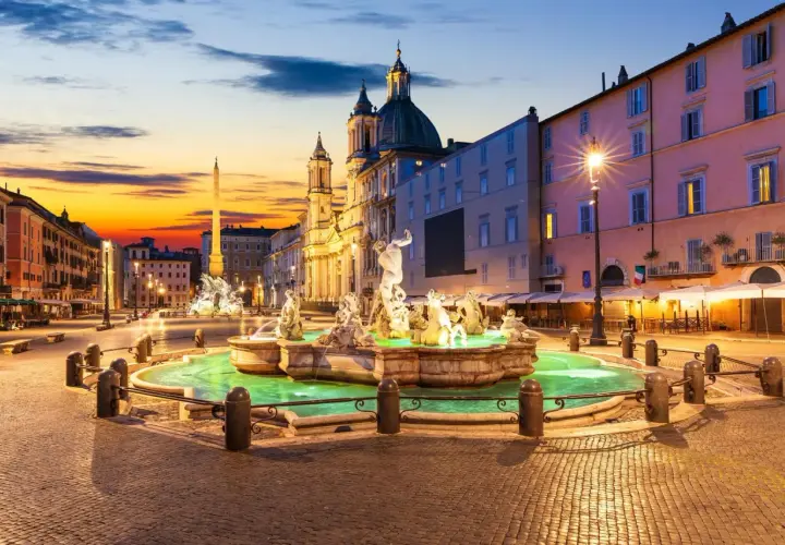 Fontaine de la piazza Navona illuminée au crépuscule, avec l'obélisque et l'église en arrière-plan.
