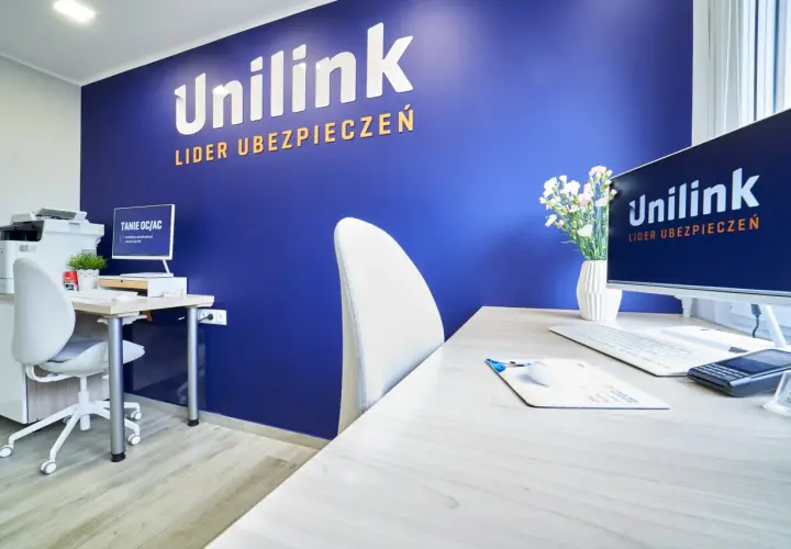 Biuro z niebieską ścianą z logo Unilink, biurkiem, komputerem i krzesłem.