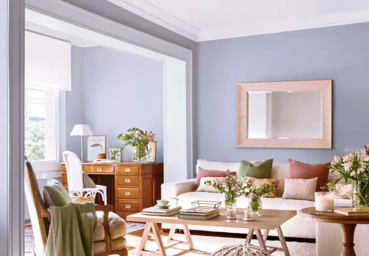 Escritorio de madera con cajonero, silla, sofá con cojines y mesa de centro en una sala de estar luminosa.