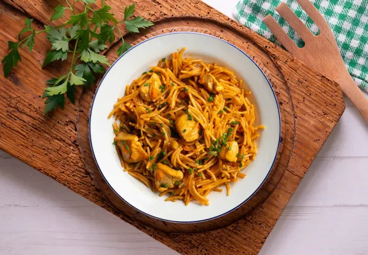 Delicioso plato de fideuà de pollo, con fideos finos y trozos de pollo tierno, decorado con perejil fresco.