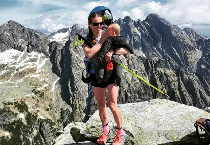 Justyna Kowalczyk z dzieckiem na szczycie górskim, w tle majestatyczne, skaliste pasmo.