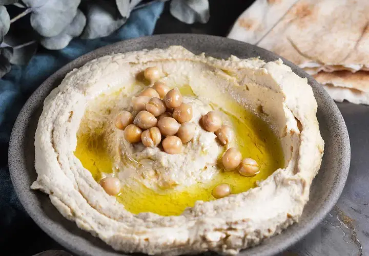 Krämig hummus med kikärtor och olivolja, perfekt för ett enkelt hummus recept. Serveras med pitabröd.