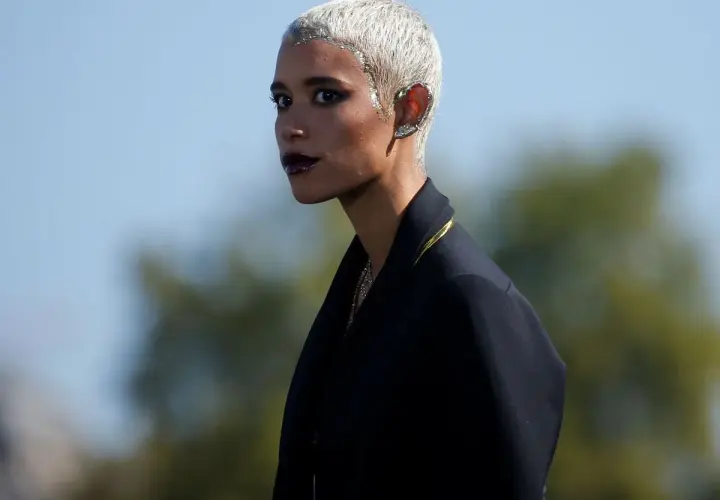 Mujer con **pelo blanco** corto y brillante, maquillaje oscuro y un pendiente llamativo en la oreja.