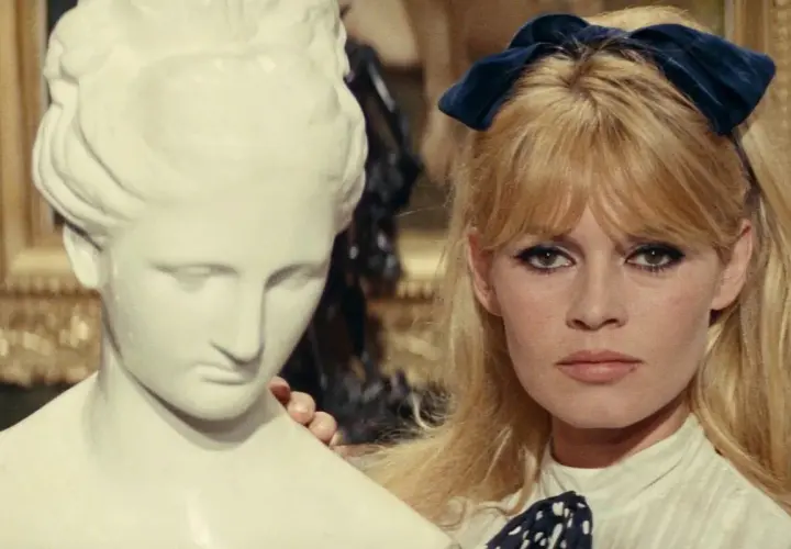 Brigitte Bardot z niebieską kokardką we włosach, obok antycznej rzeźby. Ikona lat 60 muzyka i stylu.