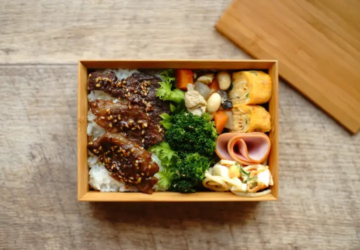 A delicious Japanese convenience store bento box filled with rice, teriyaki beef, broccoli, tamagoyaki, ham, and salad.