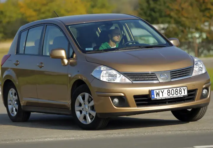 Złoty Nissan Tiida z mężczyzną za kierownicą jedzie po drodze.