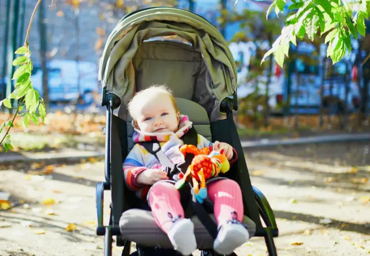 Uśmiechnięte dziecko w wózku spacerowym, gotowe na jesienne wycieczki. Czas na zmianę gondoli na spacerówkę, gdy maluch zaczyna siedzieć.