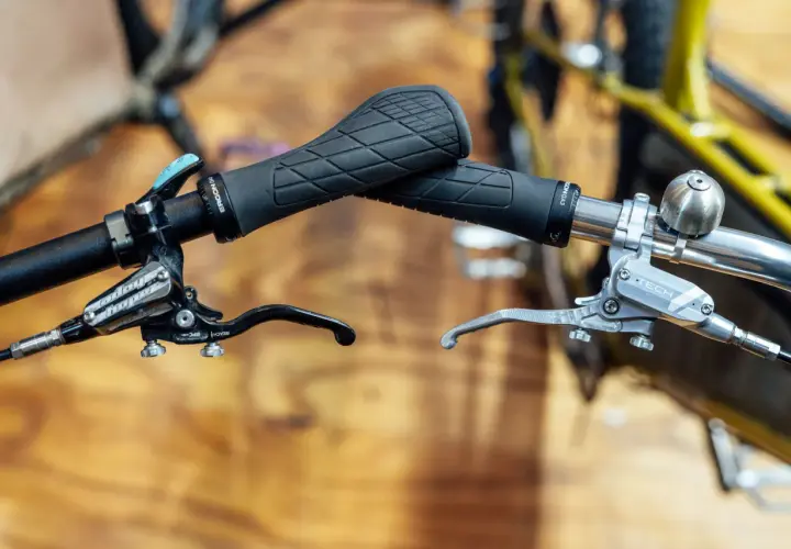 Close-up of bicycle handlebars featuring black Ergon grips and silver and black Hope e4 brakes, ready for any trail.