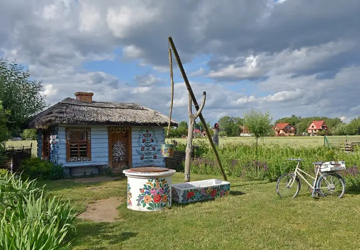 Kolorowy dom malarek w Zalipiu, z kwiecistymi zdobieniami, studnią i rowerem.