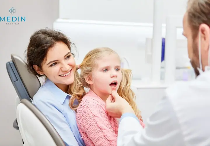 Uśmiechnięta mama towarzyszy córce podczas zabiegu lakowania zębów u dzieci. Dentysta bada jamę ustną dziewczynki.