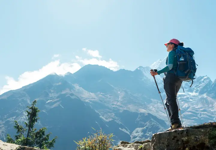 Kobieta z plecakiem i kijkami trekkingowymi podziwia majestatyczne góry. To jej wycieczka na Mount Everest, pełna wyzwań i piękna.