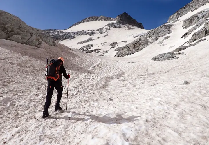 Alpinista asciende por una ladera nevada hacia el pico Aneto, con el cielo azul brillante.