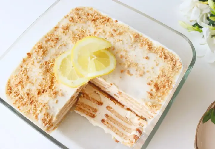 Deliciosa carlota de limón en un recipiente de vidrio, decorada con rodajas de limón y migas de galleta.