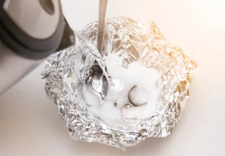 Silber putzen mit Natron: Heißes Wasser wird über Aluminiumfolie mit Natron und Schmuck gegossen, um angelaufenes Silber zu reinigen.