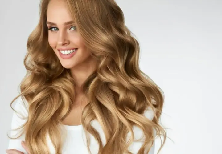 Mujer sonriente con cabello ondulado color miel rubio, que cae sobre sus hombros.