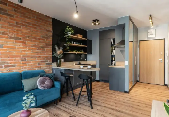 Nowoczesne mieszkanie 35m2 plan: salon z turkusową kanapą, kuchnia z wyspą i ceglaną ścianą.