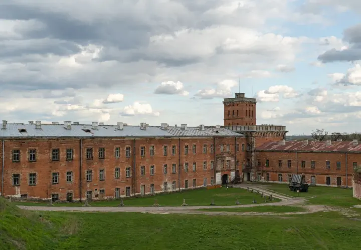 Dawny fort wojskowy w okolicach Warszawy, z ceglanymi budynkami i wieżą.