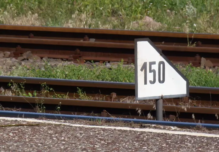 Biały trójkątny wskaźnik w11 z czarną liczbą 150 obok torów kolejowych.