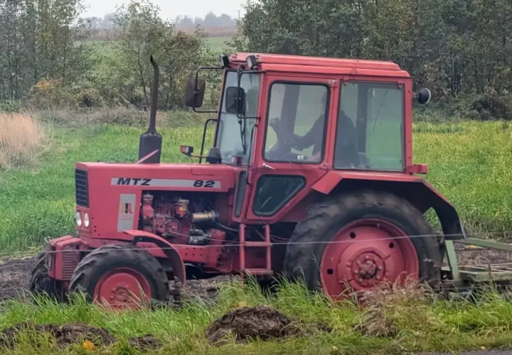 Czerwony traktor Belarus 820 pracuje na polu, za nim widać las.