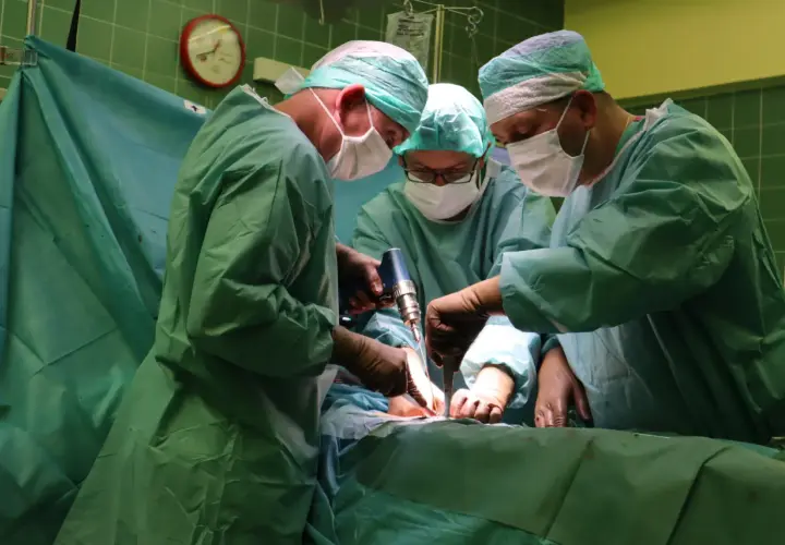 Trzech chirurgów w zielonych fartuchach i maseczkach wykonuje operację.