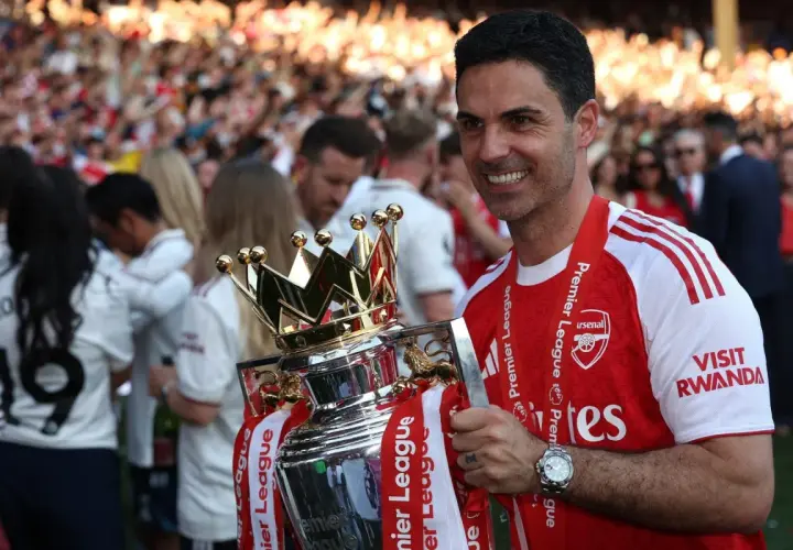 Trener Arsenalu, Mikel Arteta, z dumą trzyma puchar Premier League. Tłum kibiców świętuje sukces.
