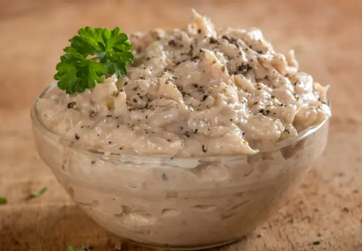 Pyszna pasta z tuńczyka, doprawiona pieprzem i udekorowana natką pietruszki, w szklanej miseczce na drewnianym tle.